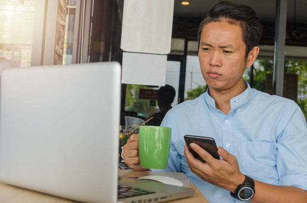 Ázsiai üzletemberek tartanak egy mobiltelefont, nézik az adatokat a számítógépen, és aggódnak a munka miatt.. - Fotó, kép