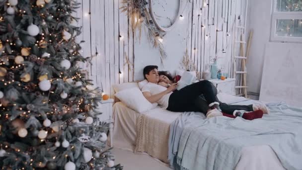 Νεαρό ρομαντικό ζευγάρι ξαπλωμένο στο κρεβάτι με ένα δώρο στο χέρι. - Πλάνα, βίντεο