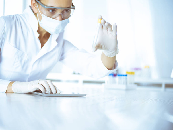 Female laboratory assistant analyzing a blood sample at hospital. Medicine, health care and researching concept - Foto, Imagen