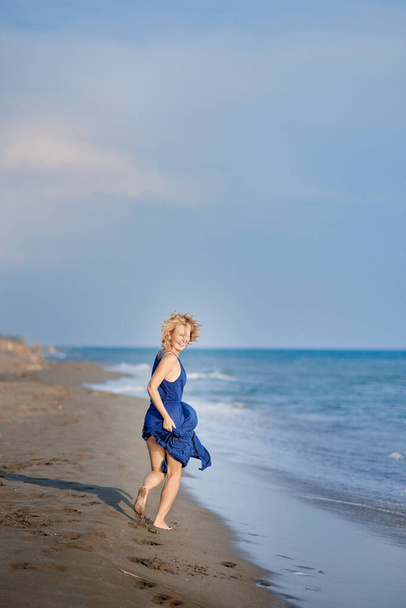 Full body portrait of a young woman laughing and running on the beach - Фото, изображение