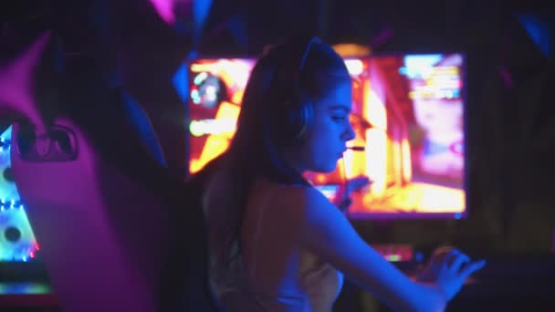 Young pretty woman sitting in neon gaming club and playing games - turns away from the monitor and looking in the camera - Footage, Video