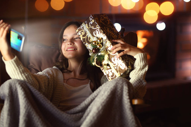 young girl takes a picture of herself with a phone with a Christmas present - Foto, Imagen