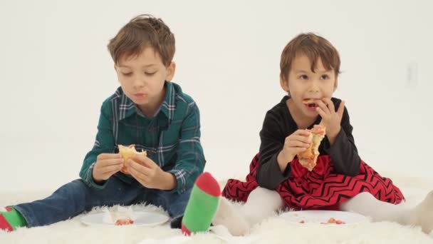 2人の子供(男の子と女の子)が白いカーペットの上に座ってホットドッグを食べる。スローモーションを閉じます - 映像、動画