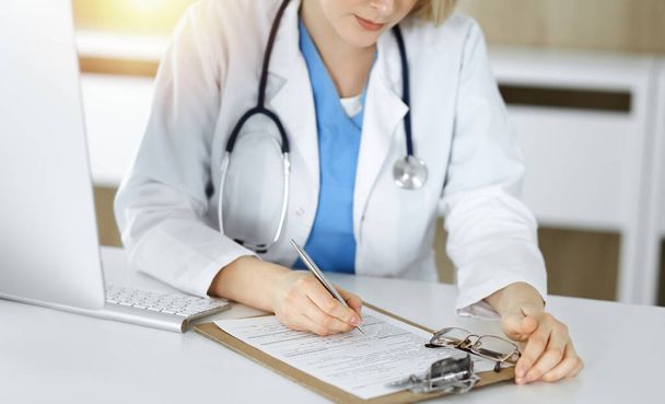 Unknown woman-doctor at work filling up medication history record form in sunny clinic, close-up - Foto, Imagem