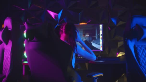 Junge hübsche Frau sitzt im neonfarbenen Spielclub und spielt Spiele - steht vom Stuhl auf und geht weg - Filmmaterial, Video