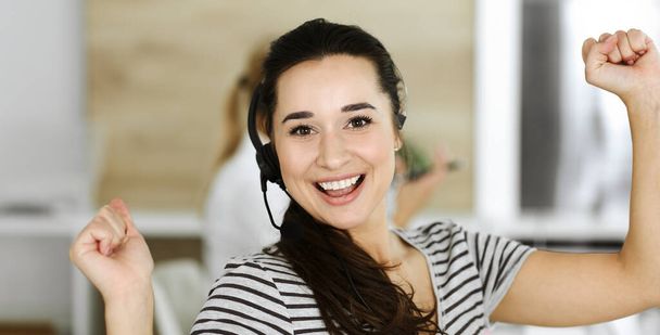 Business woman using headset for communication and consulting people at customer service office. Call center. Group of operators at work at the background. Casual dress style - Foto, afbeelding