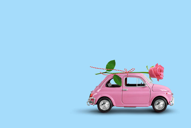 Розовая игрушечная машина доставляет розовый цветок розы на голубом фоне. Доставка цветов, женский день, день святого Валентина. - Фото, изображение