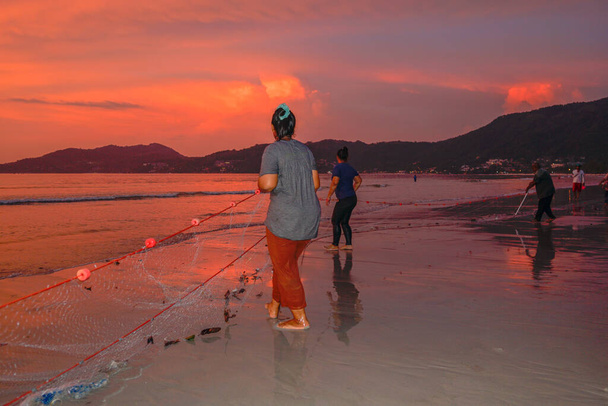 Menschen kommen heraus, um ihre Netze am Strand von Patong während des Sonnenuntergangs zu schleppen - Foto, Bild