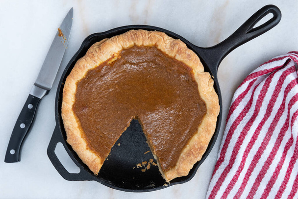 Fresh homemade pumpkin pie baked in a cast iron skillet on a kitchen counter with a slice of pie removed - Photo, Image