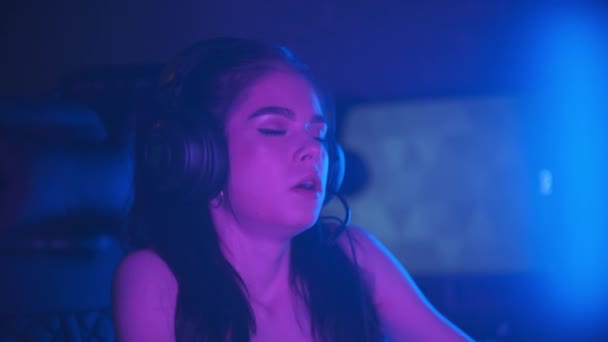 Jeune femme attrayante avec un maquillage léger assis dans le club de jeu au néon triste soupirant et tenant sa tête - Séquence, vidéo