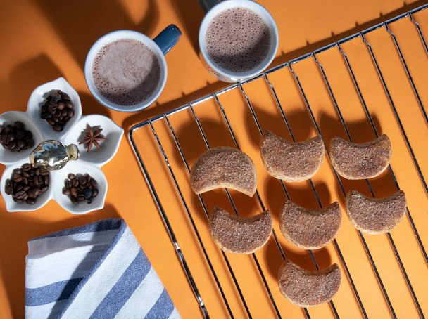 Due tazze di cacao, biscotti canditi semilunari su una griglia di metallo, asciugamano a strisce e spezie. Vista dall'alto con ombre dure - Foto, immagini