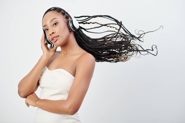 Портрет привлекательной молодой чернокожей женщины с длинными волосами, слушающей музыку в наушниках - Фото, изображение