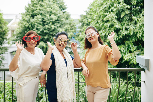 Група щасливих збуджених літніх жінок в смішних окулярах розважаються на домашній вечірці
 - Фото, зображення