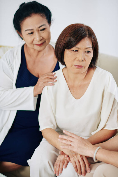 Senior Asian women reassuring their frustrated friend, touching her hands and patting on shoulder - Photo, Image