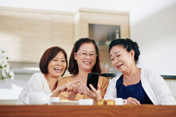 Group of cheerful Vietnamese senior women watching funny videos on smartphone screen - Photo, Image