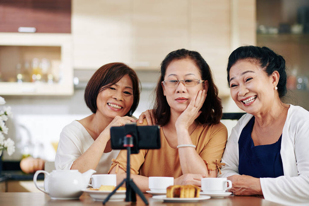 Gruppe glücklicher älterer Frauen unterhält sich am Küchentisch beim Selfie mit dem Smartphone - Foto, Bild