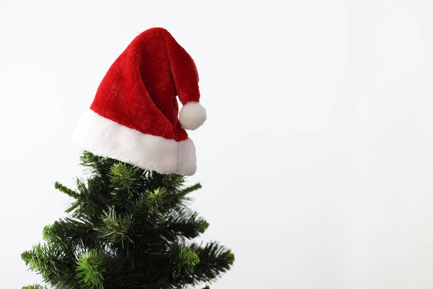 Στην κορυφή του δέντρου της Πρωτοχρονιάς κρέμεται Santa Clauss κόκκινο καπέλο close-up - Φωτογραφία, εικόνα