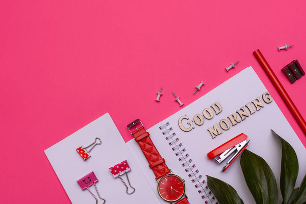 Modern office desk workplace with blank notebooks, wrist watch, pencil and office supplies on pink background. Lettering good morning. Copy space. Top view. Flat lay style.  - Photo, Image