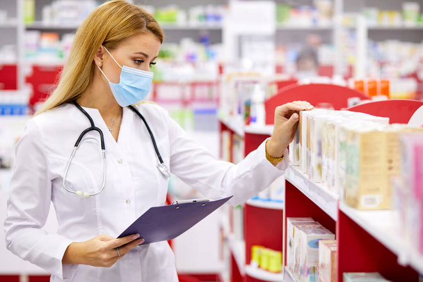 young good-looking woman pharmacist searching for medication on pharmacy shelves - Фото, зображення