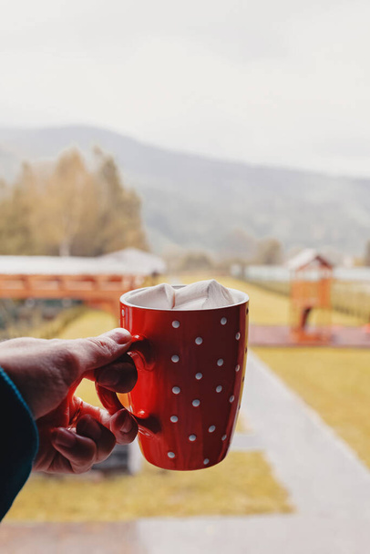 Female hand holds a cup with hot cocoa on the background of autumn backyard - Foto, Imagem