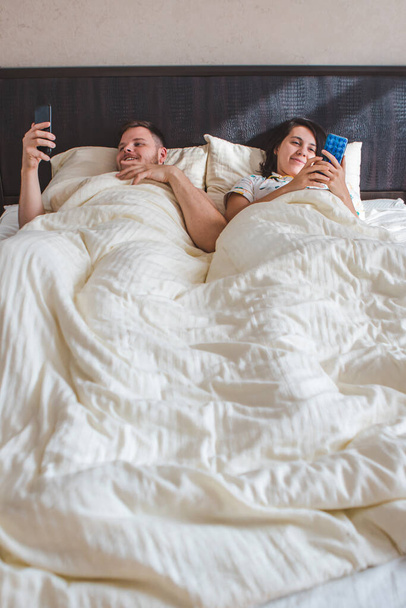 couple laying in bed surfing internet on phone modern addiction - Fotografie, Obrázek