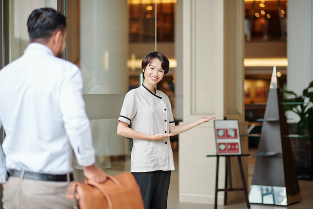 Smiling hospitable concierge welcoming guest at doors of fancy hotel - Photo, Image