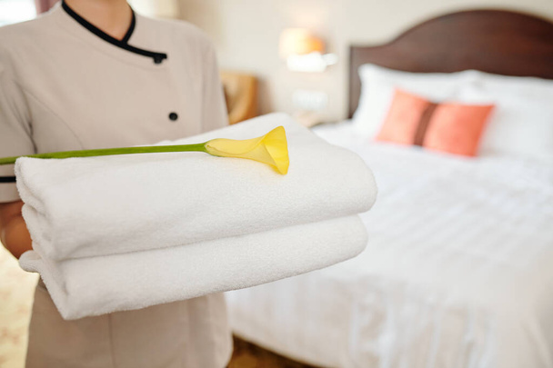 Hotel maid holding stack of fluffy white towels with yellow calla lily - Foto, Imagen