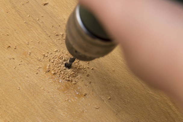 Τρυπάνι κάνει μια τρύπα σε μια ξύλινη σανίδα, θέμα των εργασιών επισκευής και την οικοδόμηση - Φωτογραφία, εικόνα