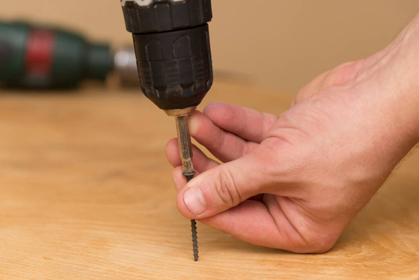 Wireless screwdriver in the hands of a man, on a wooden background, the theme of repair work and building - Photo, Image