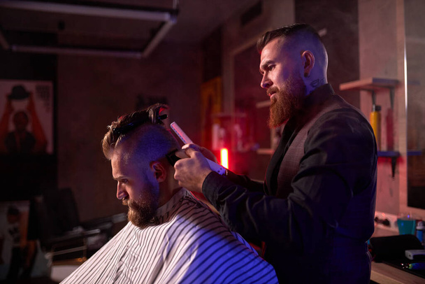 confident male hairstylist cut hair to elegant stylish man sitting in salon - 写真・画像