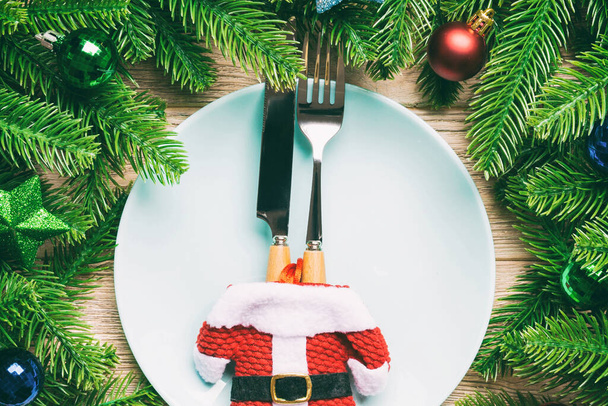 Vista superior de garfo, faca e prato cercado com abeto e decorações de Natal em fundo de madeira. Véspera de Ano Novo e conceito de jantar de férias. - Foto, Imagem