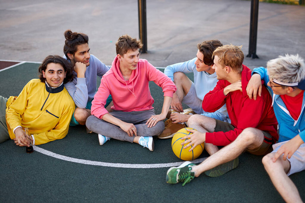 young friends sitting on basketball court, relaxing and taking break after game - Photo, Image
