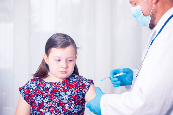 Děti očkují imunizační koncept. Lékař injekce vakcinace v paži vyděšené holčičky s obličejovou maskou. - Fotografie, Obrázek