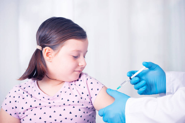 Impfkonzept für Kinder. Arzt spritzt Impfung in Arm eines kleinen Mädchens. - Foto, Bild