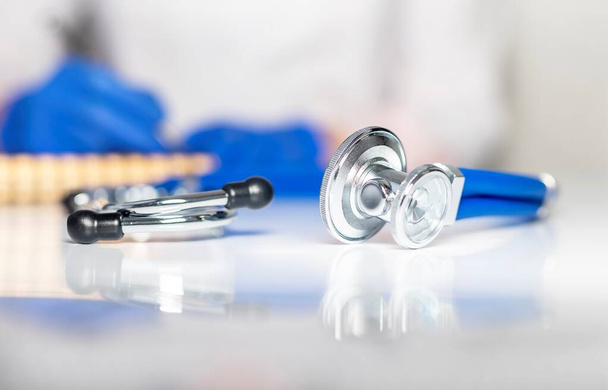 Female doctor hands write prescription at worktable. Stethoscope on foreground. close up of medical workplace. - Photo, image