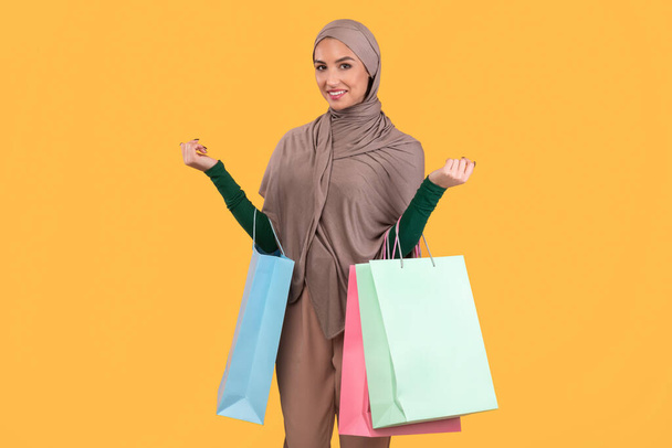 árabe dama en hijab celebración de compras bolsas sobre fondo amarillo - Foto, Imagen