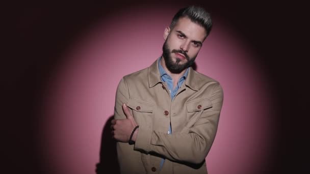 sexy jong model in denim shirt aanpassen beige jas, vasthouden arm in een mode pose, hand in hand zakken en draaien in een mode licht op roze achtergrond in studio - Video