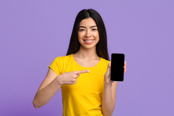Check This. Cheerful Asian Lady Pointing At Smartphone With Black Blank Screen - Foto, immagini