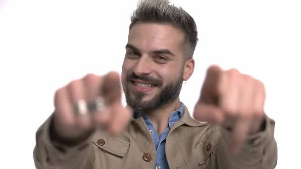 glimlachend casual model in beige jas vieren, wijzende vingers, het maken van duimen omhoog gebaar en lachen, staande geïsoleerd op witte achtergrond in studio - Video