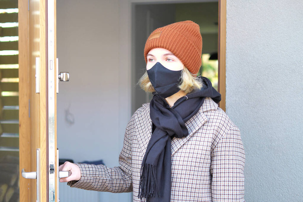 adolescente triste y preocupado con una máscara sanitaria protentiva negro entra en una casa durante el segundo encierro en coronavirus (Covid-19) pandemia - Foto, imagen