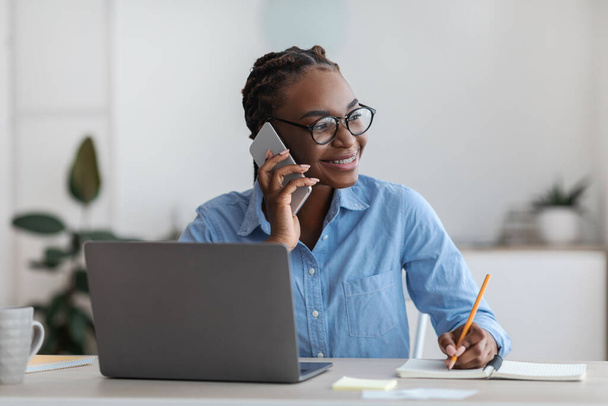 自宅オフィスで働く若い黒人フリーランスの女性と携帯電話で話す - 写真・画像