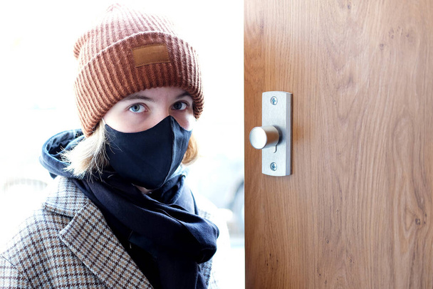 menina adolescente triste e preocupado vestindo uma máscara sanitária protentivo preto entra em uma casa durante o segundo bloqueio em coronavírus (Covid-19) pandemia - Foto, Imagem