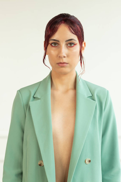 πορτρέτο ενός νέου κοριτσιού με κόκκινα μαλλιά με μακιγιάζ και σε ένα πράσινο σακάκι και jtns στο στούντιο, μόδα ομορφιά - Φωτογραφία, εικόνα