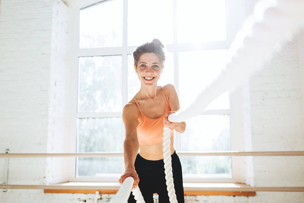 Smiling sportswoman hold battle ropes. Fitness female athlete using for workout battle ropes - Photo, Image