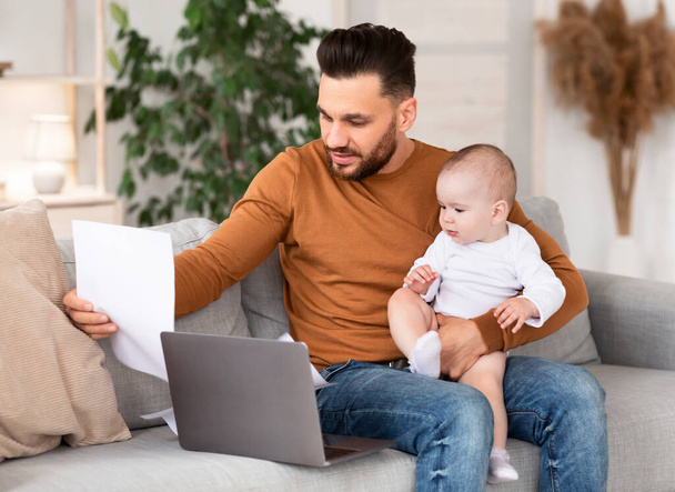 Pai com bebê trabalhando em papéis de leitura de laptop em casa - Foto, Imagem