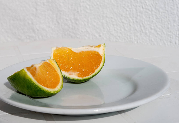 Green Tangerine cut into pieces lying on a white plate - Photo, Image