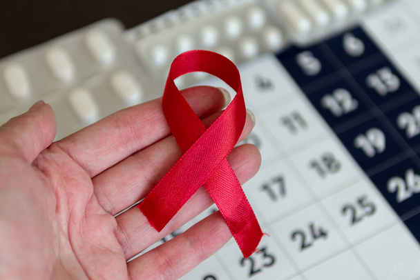 Sağlık ve tıp kavramı - takvimin arka planında AIDS hakkında kırmızı bant farkındalığı tutan kadın elleri - Fotoğraf, Görsel