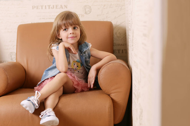 mignonne petite fille blonde s'asseoir sur un fauteuil souriant portrait rapproché sur fond intérieur rétro - Photo, image