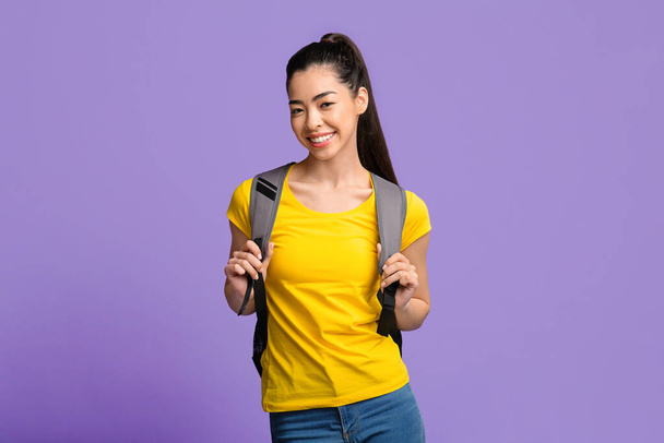 Young Beautiful Asian Female Student With Backpack Posing Over Purple Studio Background - Photo, Image