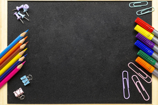 Various stationery: pencils, felt-tip pens, paper clips. School blackboard in wooden frame. Back to school and new academic year concept. Place for text, copy space - Photo, Image